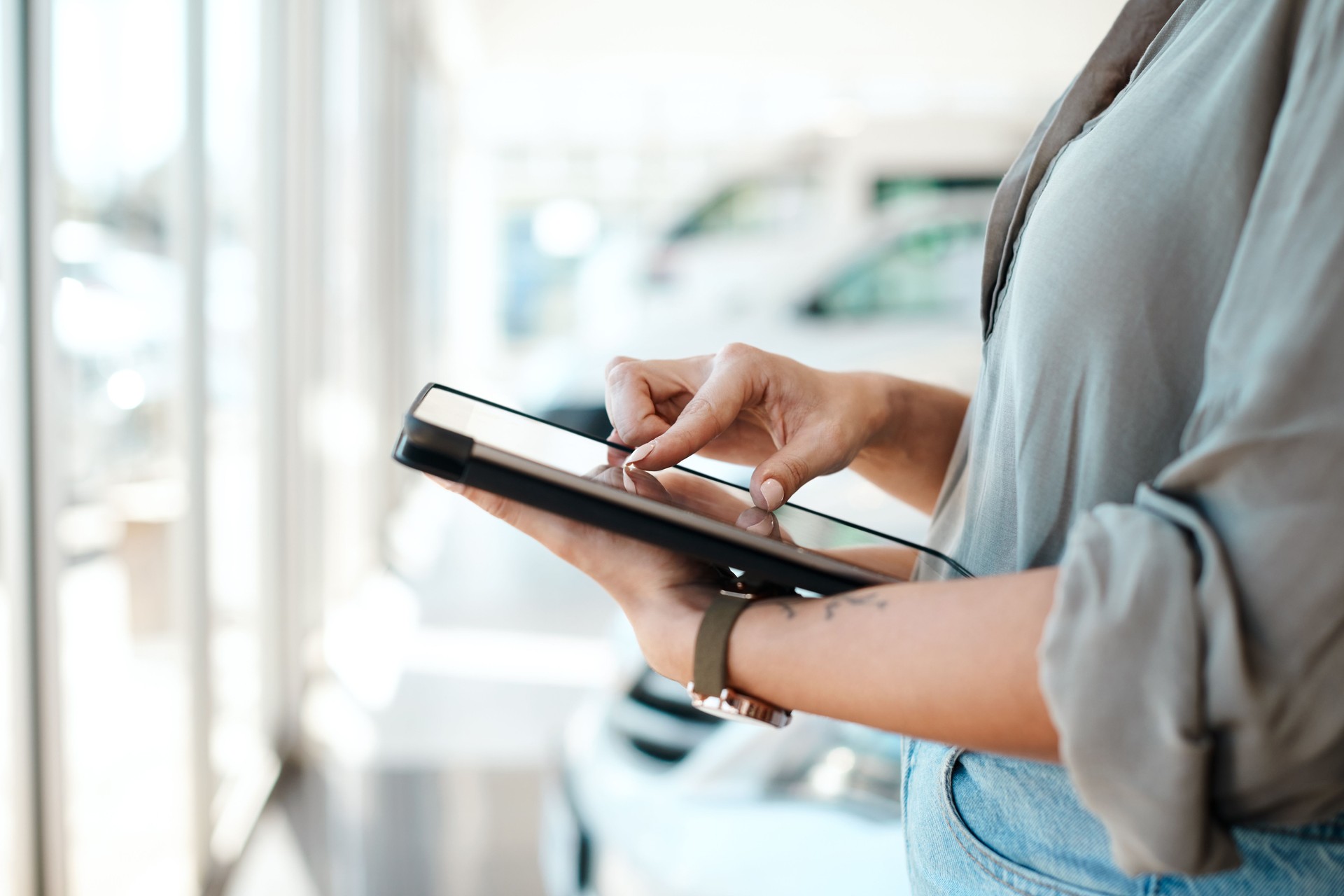 Foto de uma mulher usando seu tablet digital em uma concessionária de carros